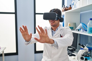 Naklejka na ściany i meble Young hispanic man scientist using virtual reality glasses at laboratory