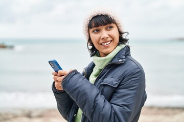 Young beautiful hispanic woman smiling confident using smartphone at seaside