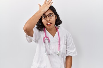 Young hispanic doctor woman wearing stethoscope over isolated background surprised with hand on...