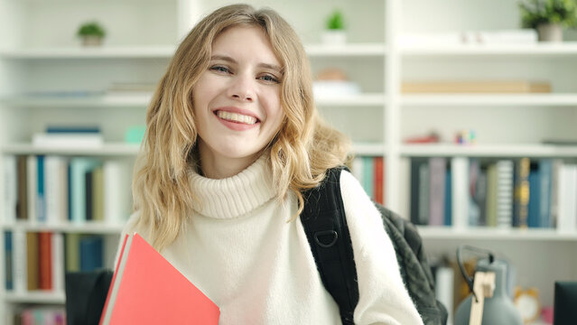Young blonde woman student smiling confident holding book at library university