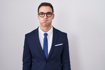 Young hispanic man wearing suit and tie puffing cheeks with funny face. mouth inflated with air, crazy expression.