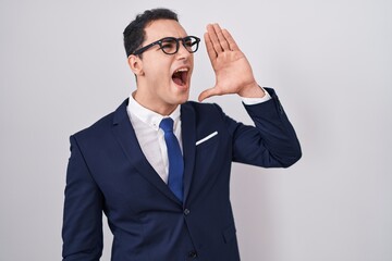 Young hispanic man wearing suit and tie shouting and screaming loud to side with hand on mouth. communication concept.