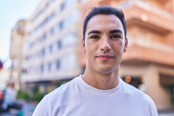 Young hispanic man standing with serious expression at street
