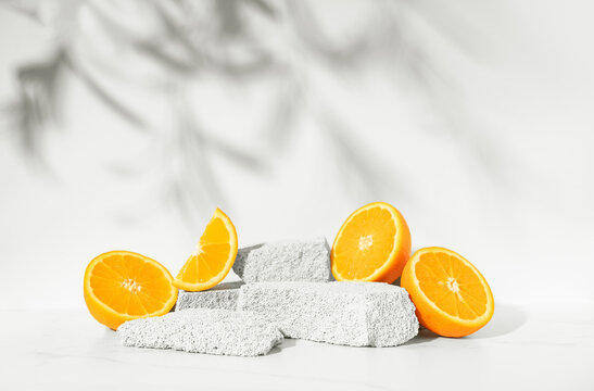 Beauty skin care product presentation podium and display made with porous stones and oranges on white sunny background. Studio photography.