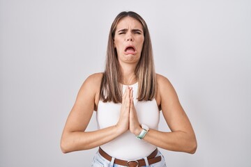Hispanic young woman standing over white background begging and praying with hands together with...