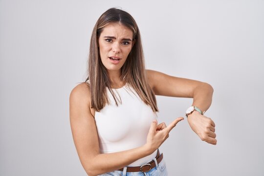 Hispanic young woman standing over white background in hurry pointing to watch time, impatience, upset and angry for deadline delay