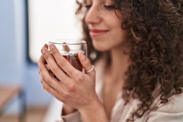 Young hispanic woman smelling tea sitting on sofa at home