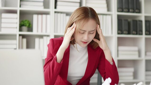 Business Woman in red suit seriously stressed working and headache due to office syndrome on laptop and paperwork in the office.