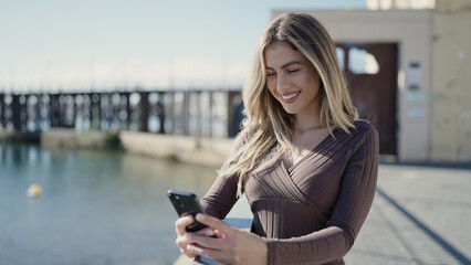 Fototapeta premium Young blonde woman smiling confident using smartphone at seaside