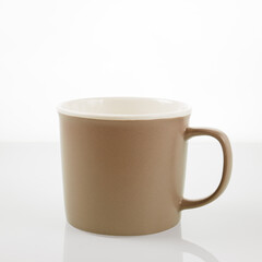 A brown ceramic mug is reflected in a glass surface