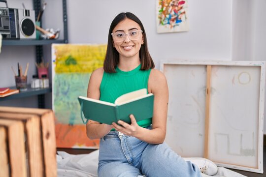 Young hispanic woman artist reading book at art studio