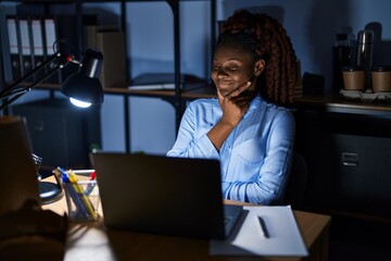 African woman working at the office at night looking confident at the camera smiling with crossed arms and hand raised on chin. thinking positive.