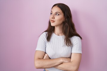 Obraz premium Young hispanic girl standing over pink background looking to the side with arms crossed convinced and confident