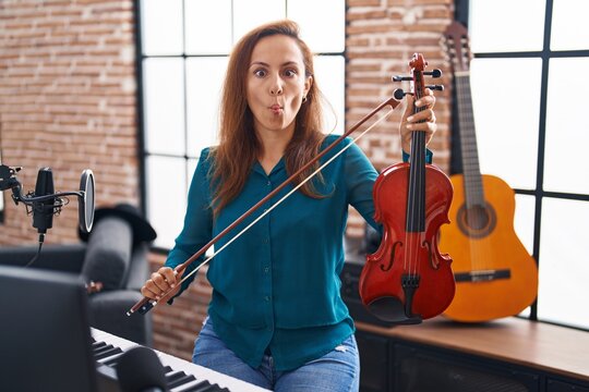 Brunette woman playing violin making fish face with mouth and squinting eyes, crazy and comical.