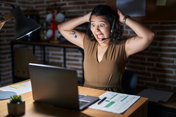 Young hispanic woman working at the office at night crazy and scared with hands on head, afraid and surprised of shock with open mouth