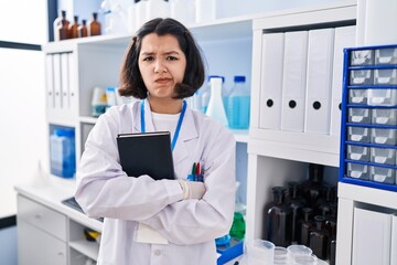 Young hispanic woman working at scientist laboratory skeptic and nervous, frowning upset because of...