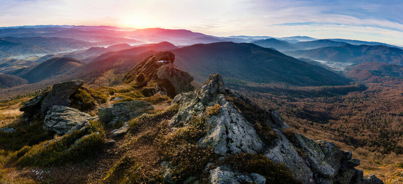 Amazing panoramic landscape of mountains range at hazy morning at sunrise. A view of the slopes of the mountains in the distance and forest hills in rays of sunlight.