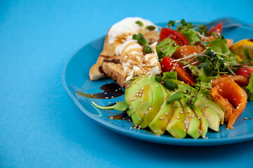 Healthy breakfast. Avocado and salmon, poached egg and toast, salad and vegetables. Microgreens on a plate. Food bowl. Lunch on a blue plate. Sauce and sesame seeds, lemon tomatoes. Top view.