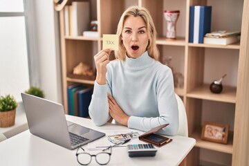Young caucasian woman calculating money savings scared and amazed with open mouth for surprise,...