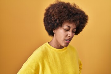 Obraz na płótnie Canvas Young african american woman standing over yellow background with hand on stomach because indigestion, painful illness feeling unwell. ache concept.