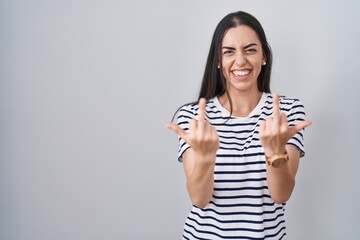 Young brunette woman wearing striped t shirt showing middle finger doing fuck you bad expression,...