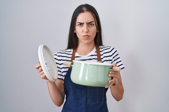 Young brunette woman wearing apron holding cooking pot skeptic and nervous, frowning upset because of problem. negative person.