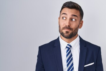 Handsome hispanic man wearing suit and tie smiling looking to the side and staring away thinking.