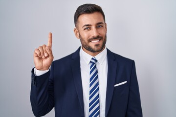 Handsome hispanic man wearing suit and tie showing and pointing up with finger number one while smiling confident and happy.