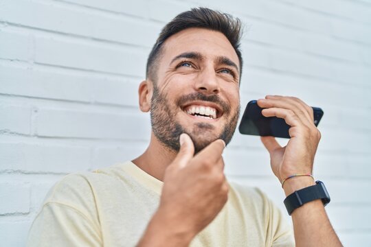 Young hispanic man smiling confident listening audio message by the smartphone over isolated white background
