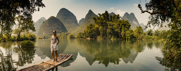 Girl standing on a raft on a Yalong River with beautiful scenery of  limestone peaks, Yangshuo,...