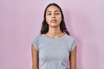 Young brazilian woman wearing casual t shirt over pink background relaxed with serious expression...