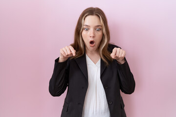 Young caucasian business woman wearing black jacket pointing down with fingers showing advertisement, surprised face and open mouth