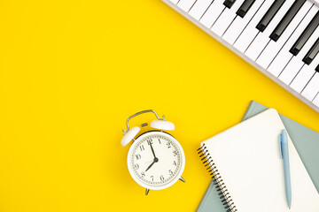 White alarm clock, notebooks and piano on a yellow background, top view, the concept of music education and creativity, white synthesizer, flat lay.