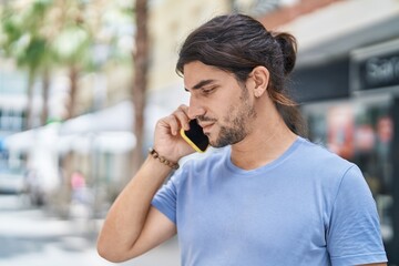 Young hispanic man talking on the smartphone at street