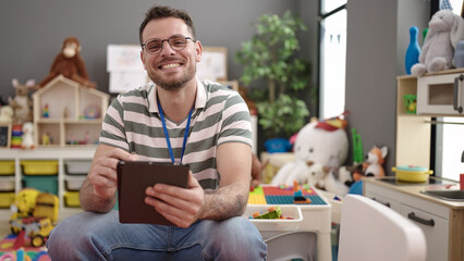 Young caucasian man working as teacher with tablet at kindergarten