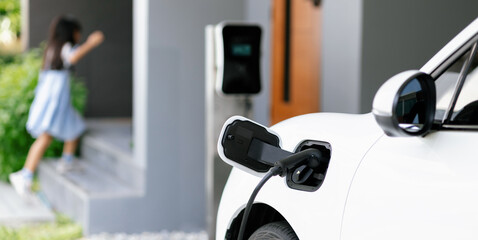 Focus EV car recharging battery at home charging station with blurred girl running in the...