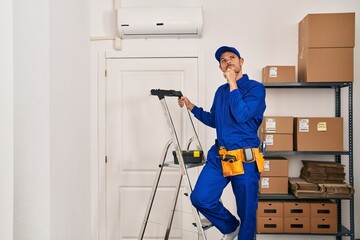Young hispanic man working at renovation serious face thinking about question with hand on chin,...