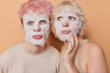 Horizontal shot of boyfriend and girlfriend apply facial sheet mask take care of skin undergo...