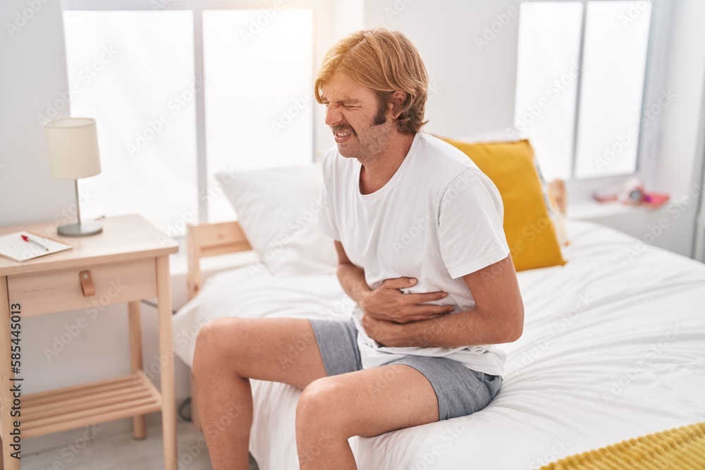 Poster Young blond man suffering for stomach ache sitting on bed at bedroom