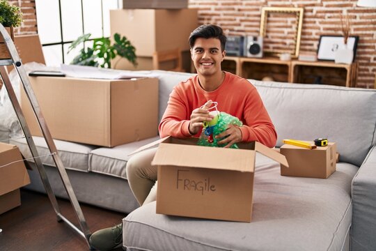 Hispanic man moving to a new home unpacking smiling with a happy and cool smile on face. showing teeth.