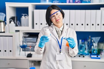 Young asian woman working at scientist laboratory relaxed with serious expression on face. simple and natural looking at the camera.