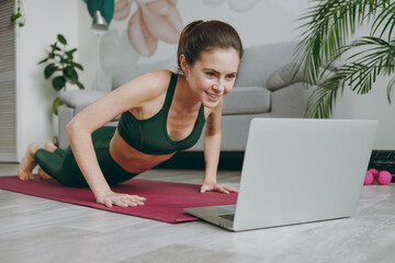 Full body young strong sporty athletic fitness trainer instructor woman wear green tracksuit do push-ups use laptop pc computer train do exercises at home gym indoor Workout sport motivation concept.