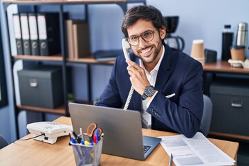 Young hispanic man business worker talking on the telephone using laptop at office