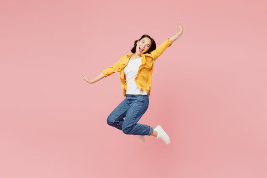 Full body side view excited young woman of Asian ethnicity wear yellow shirt white t-shirt jump high with outstretched hands look camera isolated on plain pastel light pink background studio portrait.