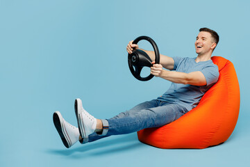 Full body side view young happy man wear casual t-shirt sit in bag chair hold steering wheel...
