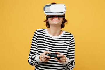 Young happy woman wears casual striped black and white shirt hold in hand play pc game with joystick console watching in vr headset pc gadget isolated on plain yellow color background studio portrait.