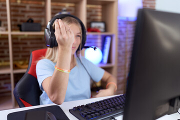 Young caucasian woman playing video games wearing headphones doing italian gesture with hand and fingers confident expression