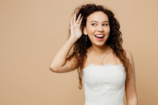 Happy young woman bride wear white wedding dress posing try to hear you overhear listening intently isolated on plain pastel light beige background studio portrait. Ceremony celebration party concept.