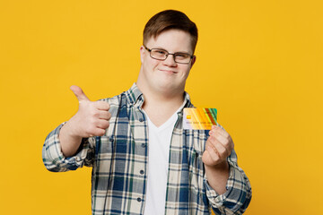 Young smiling man with down syndrome wear glasses casual clothes hold credit bank card show thumb...