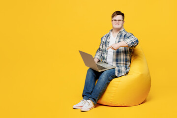 Full body young IT man with down syndrome wears glasses casual clothes sit in bag chair hold use...